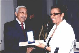 Imagem do Primeiro-Ministro ao lado da condecorada, segurando a medalha